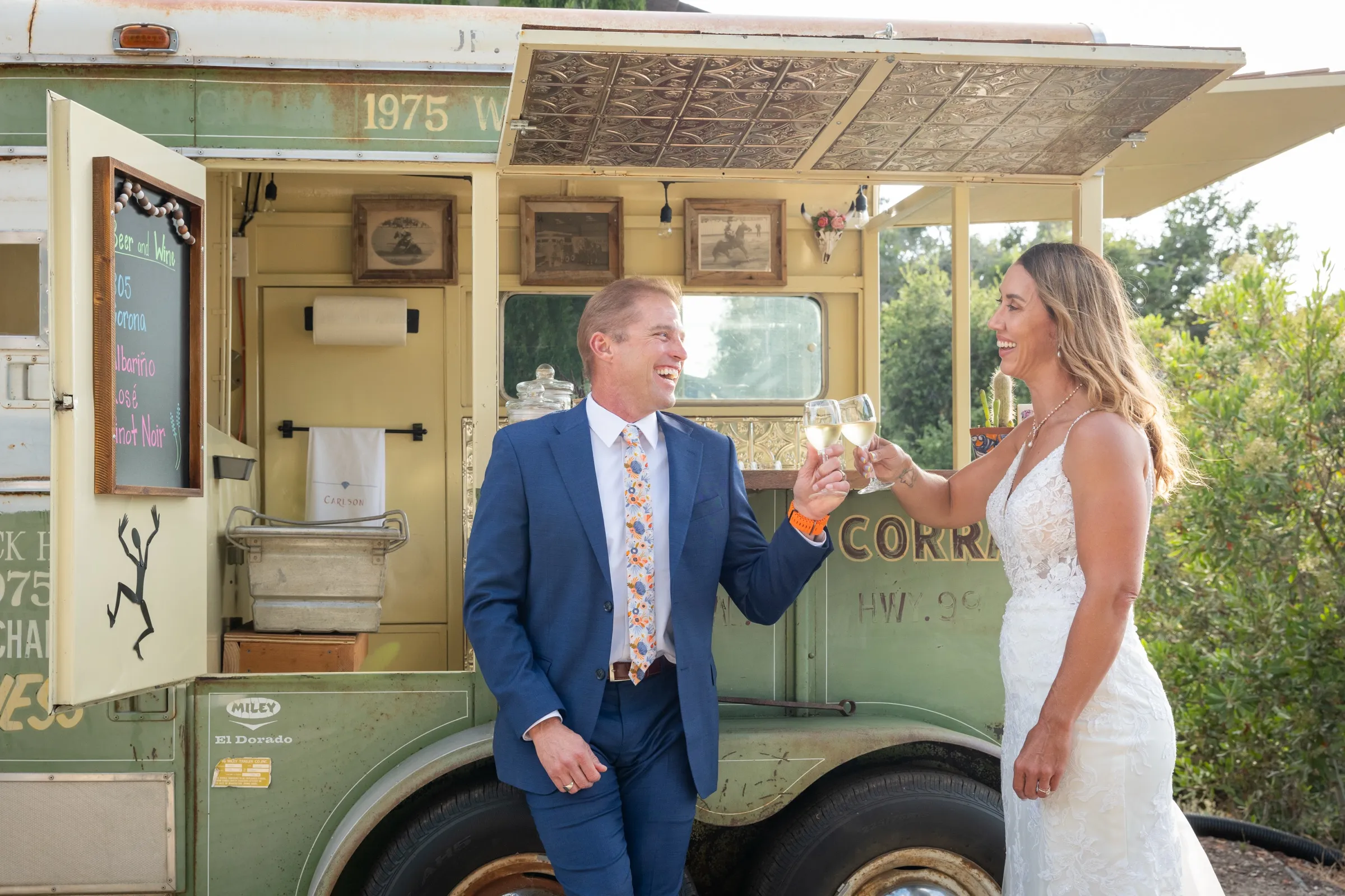 Bride and groom toasting with wine in front of a vintage bar trailer